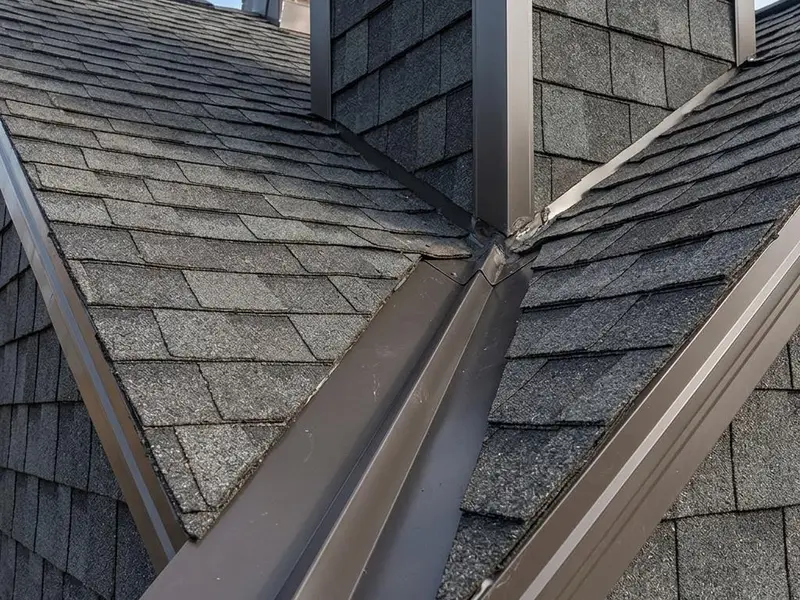 Metal drip edge and valley flashing on a shingle roof where two roof planes meet a wall